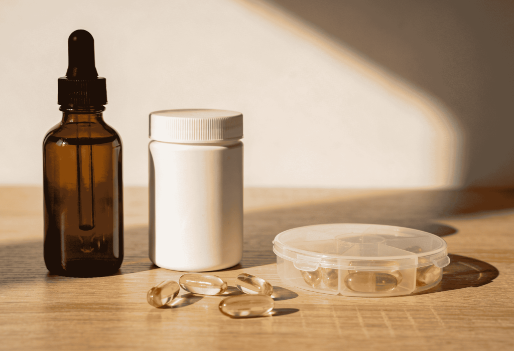 Flacon compte-gouttes ambré, pot de vitamines blanc et capsules oméga-3 dorées sur table en bois à la Pharmacie Merceron Capbreton