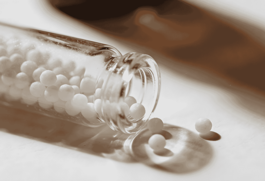 Tube de granules homéopathiques renversé avec petites billes blanches sur surface claire à la Pharmacie Merceron Capbreton