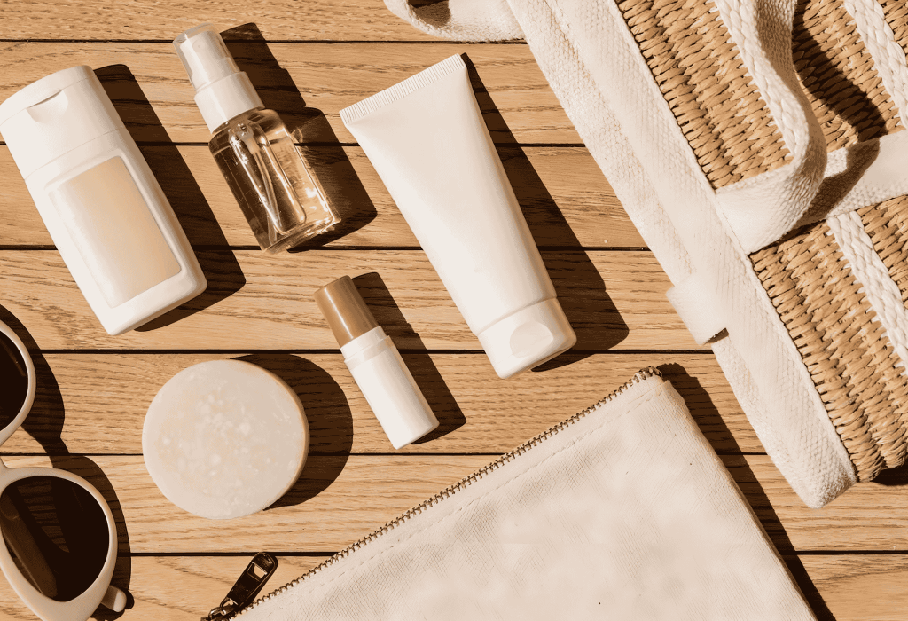 Kit voyage avec mini-formats soins essentiels, trousse et lunettes de soleil sur table en bois à la Pharmacie Merceron Capbreton